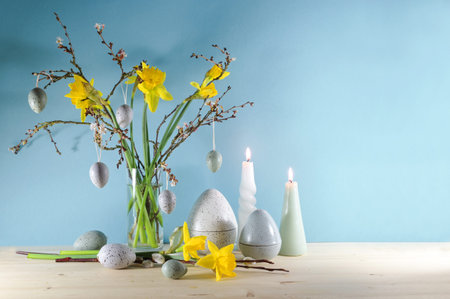 Seasonal holiday decoration with candles, a bouquet of daffodils and spring branches in a glass vase...