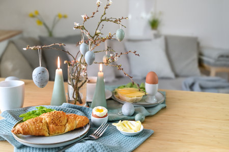 Breakfast table with boiled egg, croissant and pastel turquoise Easter decoration in a small living room, copy space, selected focus, narrow depth of fieldの写真素材