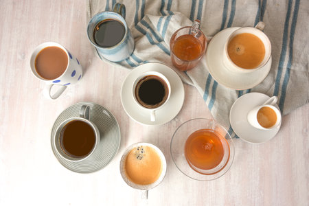 Several different cups and mugs with coffee and tea drinks on a light table with a blue gray towel, high angle view from above, selected focus, narrow depth of fieldの写真素材