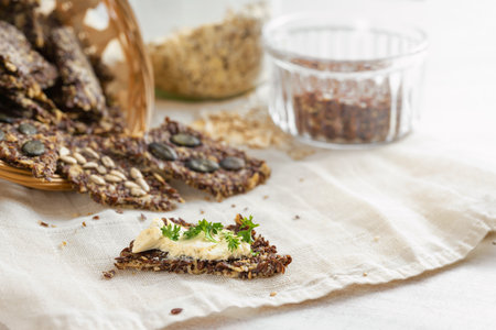 Healthy crispy snacks baked from linseed, oat flakes and various seeds, one with butter and parsley garnish on a light napkin and a table, copy space, selected focus, narrow depth of fieldの写真素材