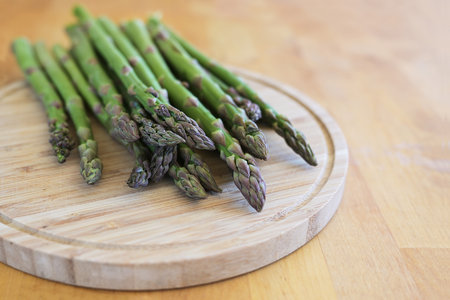 Fresh green asparagus on a cutting board and a wooden table, delicious spring time vegetables, copy space, selected focus, narrow depth of fieldの写真素材