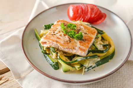 Fried wild salmon with parsley garnish on zucchini vegetables and fresh tomato on a light plate, healthy meal for a low carb diet, selected focus, narrow depth of fieldの写真素材