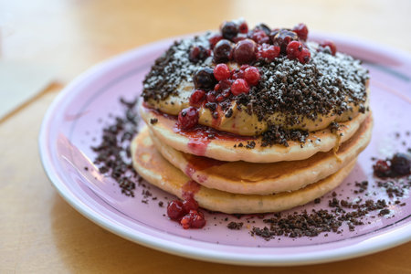 Stacked pancakes with peanut butter cream, berries, crumble and icing sugar on a plate, sweet breakfast, brunch or dessert dish, selected focus, narrow depth of fieldの写真素材