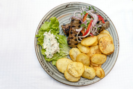 Mediterranean minced meat rolls with fried potato slices, salad and dip on a plate, white table, high angle view from above, copy space, selected focus, narrow depth of fieldの写真素材