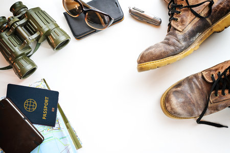 Trekking boots, binoculars, passport and other accessories for hiking vacation, flat lay on a light background, copy space, selected focusの写真素材