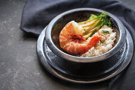 Fried giant prawn or shrimp with rice and pak choi in a black spotted ceramic bowl on a dark background, cooking in Asian style, copy space, selected focus, narrow depth of fieldの写真素材