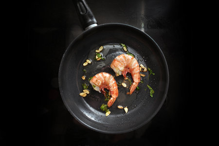 Frying jumbo tiger prawns in olive oil with garlic and herbs in a pan on a black stove top, cooking a gourmet seafood meal with fresh crustaceans, top view from above, copy space, selected focusの写真素材