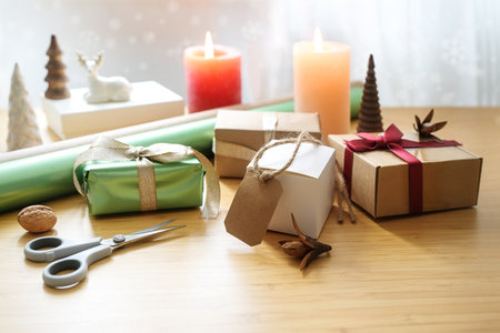 Present wrapping, wooden table with gifts, scissors, paper, candles and Christmas decoration, holiday activity at home, copy space, selected focus, narrow depth of fieldの写真素材
