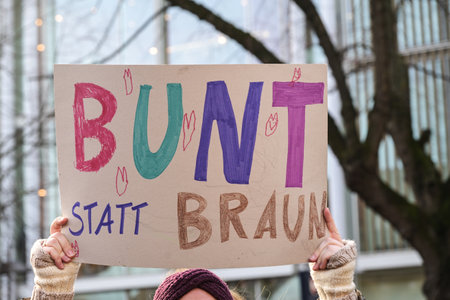 Woman holding a cardboard sign with the German text Bunt Statt Braun (Colorful instead of Brown), as protest against racism and neo-Nazi fascism on a demonstration in Lubeck Germany, January 22, 2024の写真素材