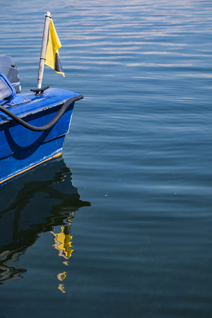Stern of a blue boat with a yellow flag reflected in calm water with small waves, concept for summer vacations, water sport and leisure activity, large copy space, selected focusの写真素材