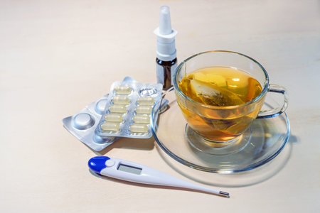 Hot tea, pills, nasal spray and fever thermometer, medical treatment against colds and flu on a...