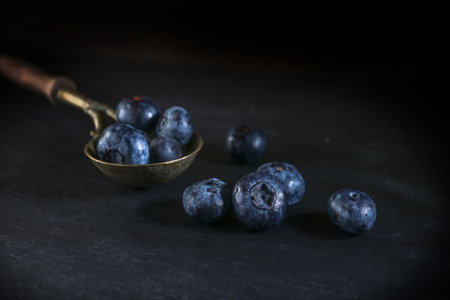 Vintage brass spoon with blueberries on a black slate plate, dark and moody still life with fruits, copy space, selected focus, narrow depth of fieldの写真素材