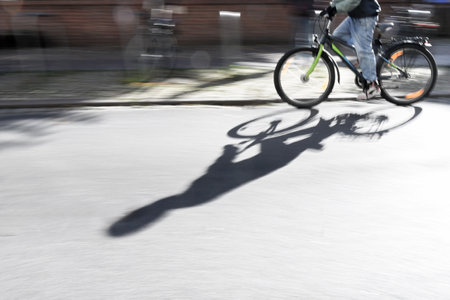 Part of a young man riding a bicycle on the street in the city, casting a long shadow on the asphalt, panning photography with motion blur, copy spaceの写真素材