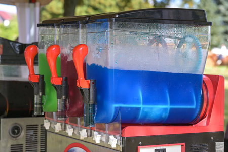 Slush machine making colorful frozen drinks with different flavors, refreshing beverages with ice in blue, red and green at a funfair market, selected focusの写真素材