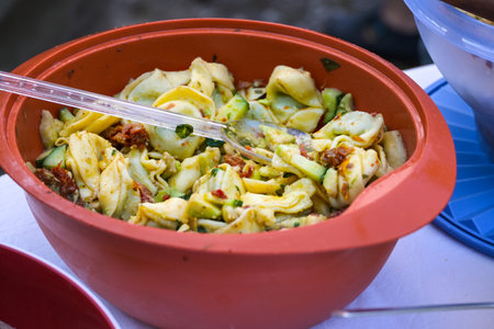 Tortellini salad in a red plastic bowl, homemade for picnic or an outdoor party, selected focus, narrow depth of fieldの写真素材