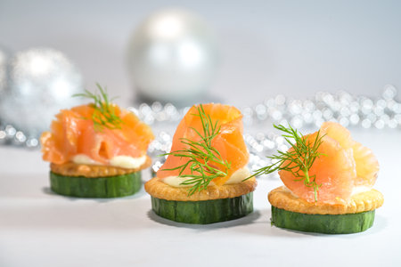 Finger food from smoked salmon on cucumber slices and crackers with dill garnish, Christmas decoration in the gray background, festive party snack, copy space, selected focus, narrow depth of fieldの写真素材