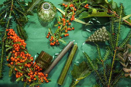 Green flat lay of candles, Christmas decoration, evergreen twigs and red orange berries, seasonal holiday background, high angle view from above, selected focusの写真素材