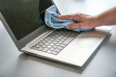 Hand cleaning a dusty laptop with a blue cloth, hygiene at the workplace maintains health,...