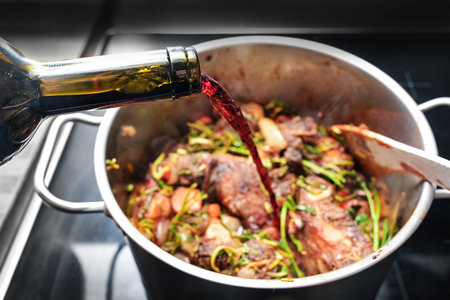 Pouring red wine into a stainless steel pot to deglaze the roasted ingredients such as meat, vegetables and herbs, cooking a tasty stew, selected focus, narrow depth of fieldの写真素材