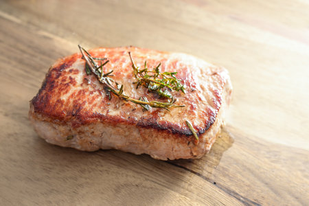 Pork loin steak roasted with herbs and served on a wooden board, tasty meat from the barbeque grill, copy space, selected focus, narrow depth of fieldの写真素材
