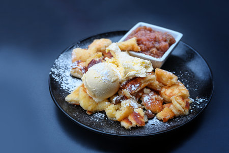 Kaiserschmarrn, fluffy shredded pancake with vanilla ice cream and fruit compote on a dark blue plate, popular dessert in Austria and Bavaria, copy space, selected focus, narrow depth of fieldの写真素材