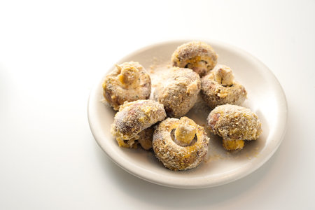 Breaded mushrooms on a white plate, ready to be deep fried or baked in the oven, preparation for a party snack from vegetables, copy space, selected focus, narrow depth of fieldの写真素材