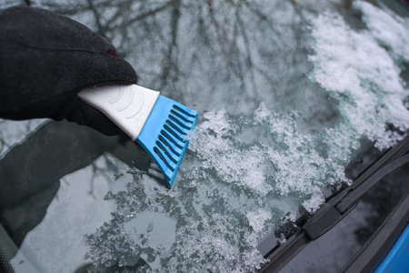 Hand with an ice scraper cleaning the car windshield from frozen snow, important tool for save driving, concept for traffic in winter, copy space, selected focus, narrow depth of fieldの写真素材