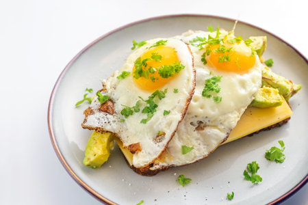 Crispy fried eggs on dark wholemeal bread with cheese, avocado and parsley garnish on a gray plate,...