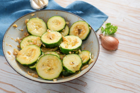 Zucchini slices marinated in oil, garlic, onion, spices and herbs, cooking with vegetables for a healthy vegetarian and vegan meal, blue napkin, light wooden table, copy space, selected focus, narrow depth of fieldの写真素材