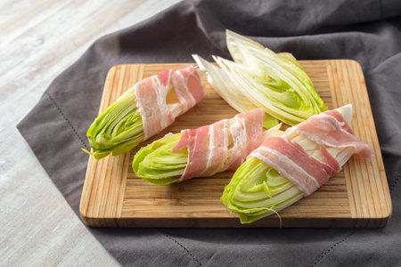 Halved chicory wrapped in strips of bacon prepared to be fried or baked in the oven on a kitchen...