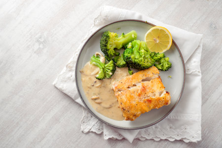 Fried cod fish fillet with broccoli, sauce and a slice of lemon on a gray plate and a white painted wooden table, healthy meal for a low carb diet, high angle view, copy space, selected focusの写真素材