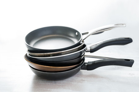 Stack of various frying pans made from cast iron, carbon steel, non-stick coated and stainless steel, choosing the right kitchen ware, light gray background, copy space, selected focusの写真素材