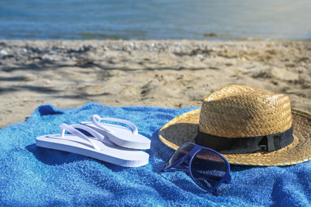 Straw hat, flip flops and sunglasses on a blue towel on a natural beach of the Baltic Sea on a sunny...