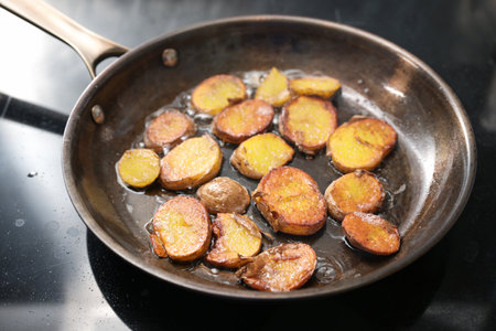 Crispy fried slices of potatoes with plenty of oil in a seasoned iron frying pan, rustic vegetarian meal, selected focus, narrow depth of fieldの写真素材