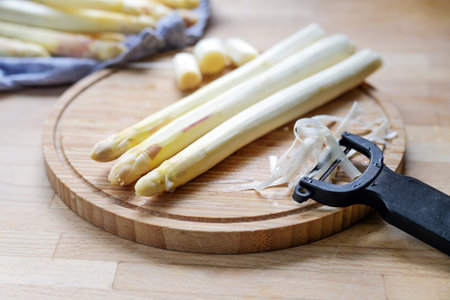 White asparagus is peeled on a wooden cutting board in the kitchen, healthy cooking with seasonal vegetables, copy space, selected focus, narrow depth of fieldの写真素材