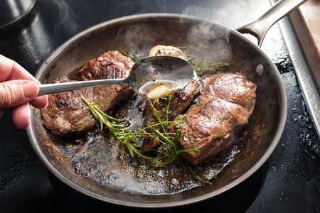 Freshly roasted beef steaks are napped with butter garlic, thyme and rosemary in a carbon steel frying pan, homemade cooking a tasty meat meal, selected focus, narrow depth of fieldの写真素材