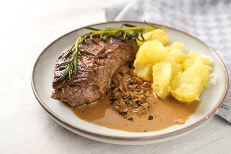 Roasted beef steak with boiled potatoes, sauce and herb garnish on a plate and a white wooden table, homemade meat meal, copy space, selected focus, narrow depth of fieldの写真素材