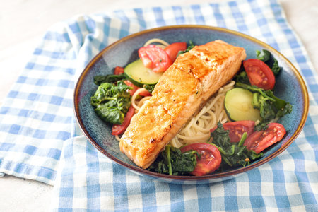Salmon fillet on spaghetti with spinach, zucchini and tomatoes served in a blue plate on a napkin, healthy protein meal, copy space, selected focus, narrow depth of fieldの写真素材