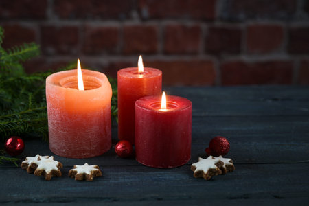 Tree red candles, some cookies, baubles and fir branches against a dark brick wall, decoration or greeting card for Christmas, Advent or New Year, large copy space, selected soft focus