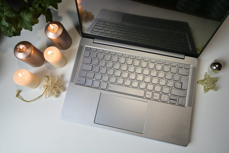 Laptop with candles and some Christmas decorations on a light office desk, holiday business or cozy...