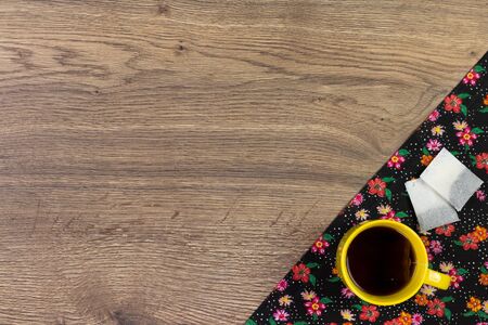 Tea mug on pattern flower cloth napkin on empty wooden background. Top view with space for your text.の写真素材