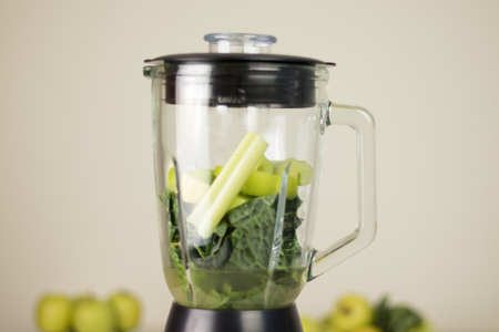 Blender jar with green leaves, celery and apples. Fruits and vegetables on blurry background. Detox juice preparation ingredients.の写真素材