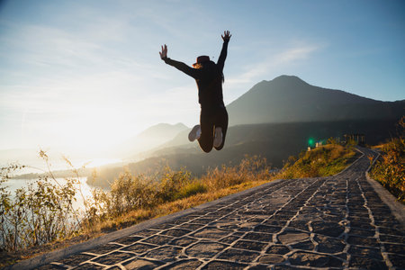 Young woman jumping with her hands up in front of Lake Atitlan watching the sunrise - young traveler jumping excited at the viewpoint of San Juan la Laguna Guatemalaの写真素材