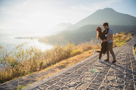 Traveler couple embracing in the middle of a road at sunrise with Lake Atitlan behind them - Hispanic couple in love with volcanoes and mountains landscape behind them - Adventurous couple in Guatemalaの写真素材