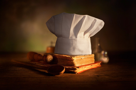 Old culinary books , chef hat and wooden spoons . Kitchen accessories on the old wooden table .の写真素材