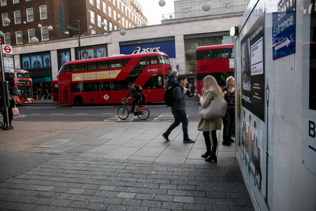 A girl waiting at the street when passing a double decker bus