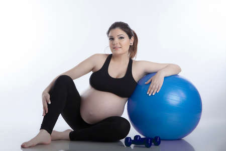 Pregnant woman is doing exercises with gymnastic ball on white backgroundの写真素材