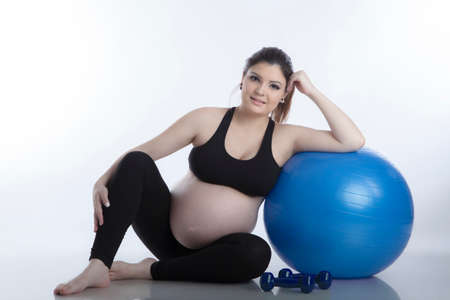 Pregnant woman is doing exercises with gymnastic ball on white backgroundの写真素材