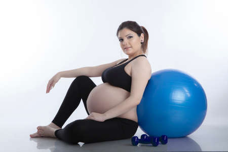 Pregnant woman is doing exercises with gymnastic ball on white backgroundの写真素材