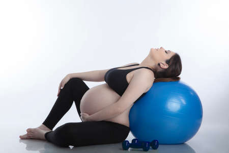 Pregnant woman is doing exercises with gymnastic ball on white backgroundの写真素材